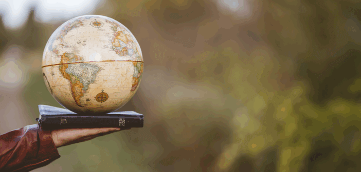 Photo of an outstretched hand holding a globe atop a Bible while in a country setting