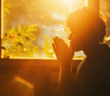 Person praying in front of a window with morning sunshine pouring in