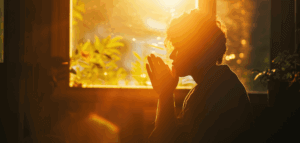 Person praying in front of a window with morning sunshine pouring in