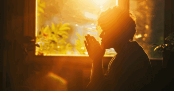 Person praying in front of a window with morning sunshine pouring in