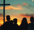 Silhouette of people watching the sun rise at an outdoor sunrise service with a large cross in the background