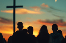 Silhouette of people watching the sun rise at an outdoor sunrise service with a large cross in the background