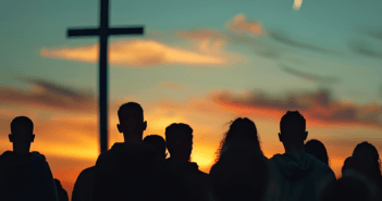 Silhouette of people watching the sun rise at an outdoor sunrise service with a large cross in the background