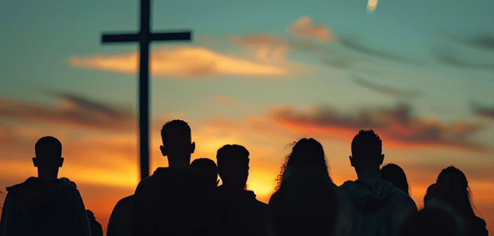 Silhouette of people watching the sun rise at an outdoor sunrise service with a large cross in the background