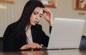 Person at a desk looking uneasily at a laptop computer