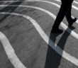 Person and their shadow walking on pavement painted with wavy lines