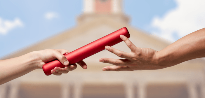 Two people's hands passing a baton from one to the other in front of a blurred image of a church