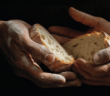 The hands of two people together holding slices of rustic bread