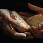 The hands of two people together holding slices of rustic bread