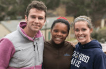 Three smiling teenagers outside on a mission trip to the country