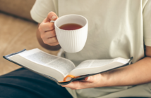 Person sitting on a couch reading a book while drinking a cup of hot tea