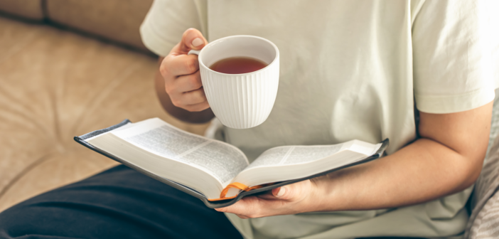 Person sitting on a couch reading a book while drinking a cup of hot tea
