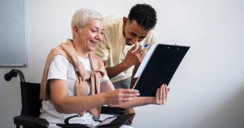 Older person in a wheelchair smiling while sharing information with a younger team member