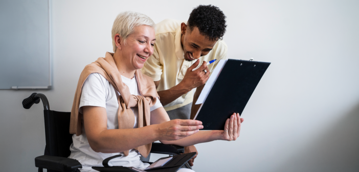 Older person in a wheelchair smiling while sharing information with a younger team member
