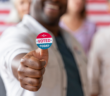 Smiling person with an I VOTED sticker accompanied by other voters