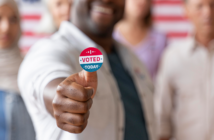 Smiling person with an I VOTED sticker accompanied by other voters