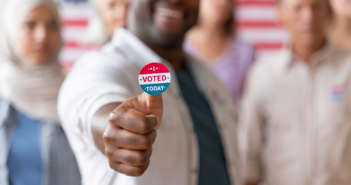 Smiling person with an I VOTED sticker accompanied by other voters