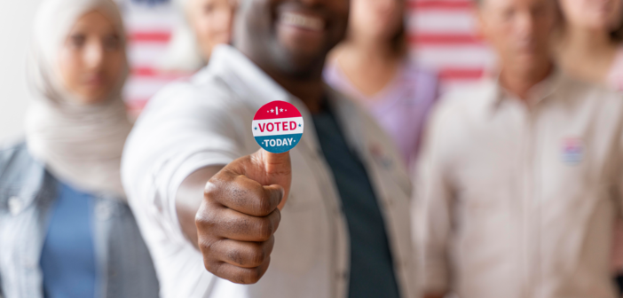 Smiling person with an I VOTED sticker accompanied by other voters