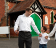 Smiling childholding the hands of their smiling parents outside of a church building