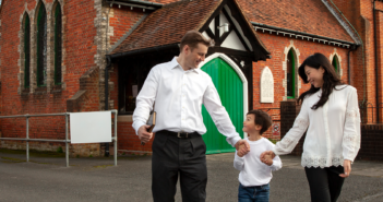 Smiling childholding the hands of their smiling parents outside of a church building