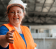 Construction worker in a hard hat and orange safety vest reaching out their hand to you in a room under construction