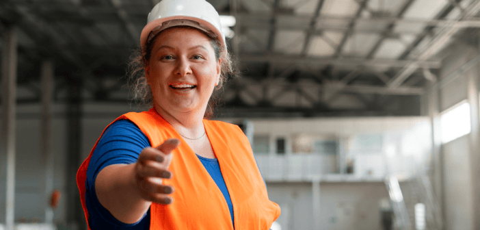 Construction worker in a hard hat and orange safety vest reaching out their hand to you in a room under construction