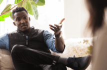 Person sitting on a couch with their legs crossed having a difficult conversation with another person