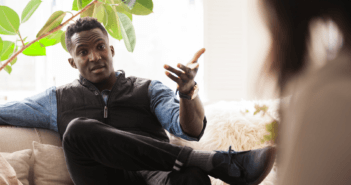 Person sitting on a couch with their legs crossed having a difficult conversation with another person