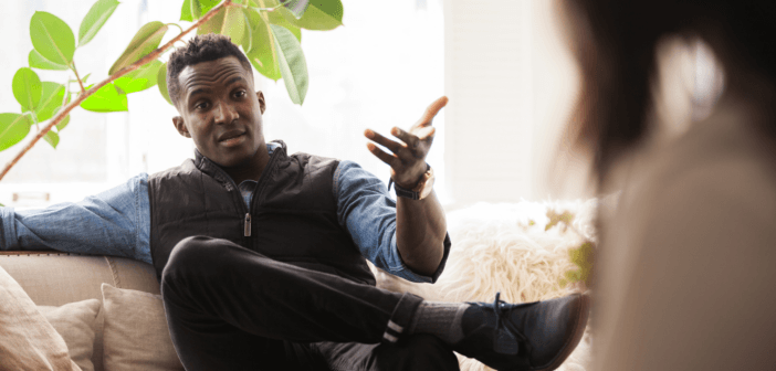Person sitting on a couch with their legs crossed having a difficult conversation with another person
